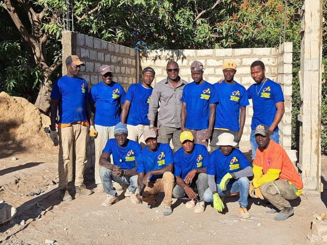 L'équipe en tee-shirts bleus à l'effigie de l'entreprise, devant un mur en parpaings en cours de construction